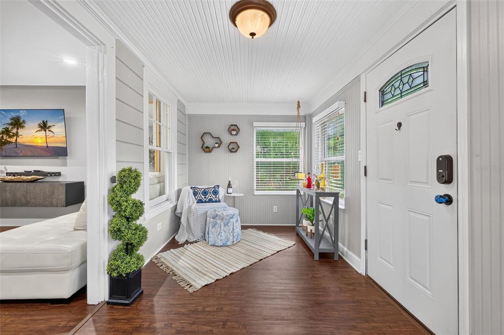 A sunroom with gray beadboard walls, wood-look flooring, a white front door, and a chair — 920 29TH STREET N, ST PETERSBURG, FL