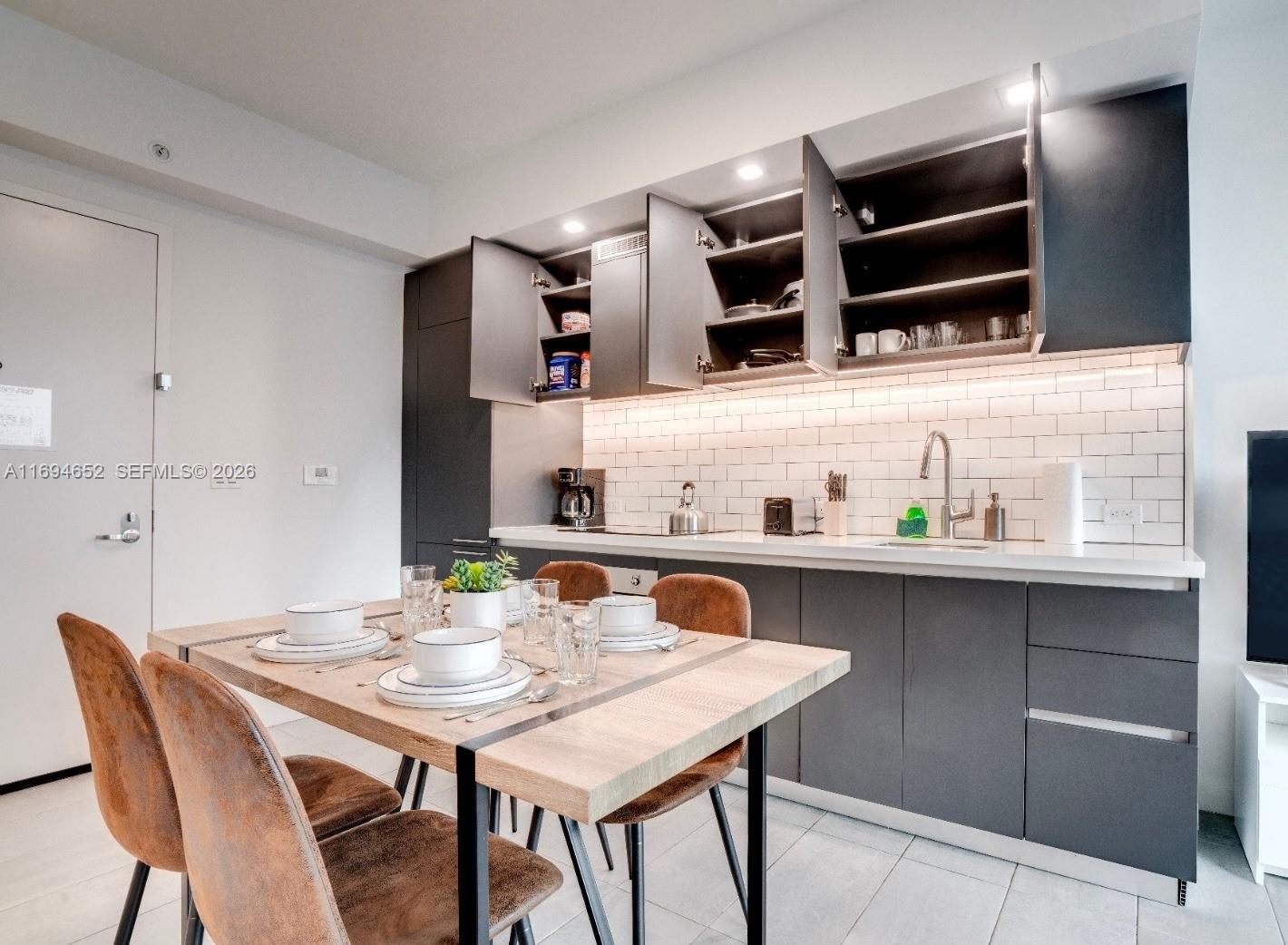 A modern kitchen features dark gray cabinets, white subway tile backsplash, and a wooden dining table — 227 NE 2nd St # 1705, Miami FL 33132, MIAMI, FL