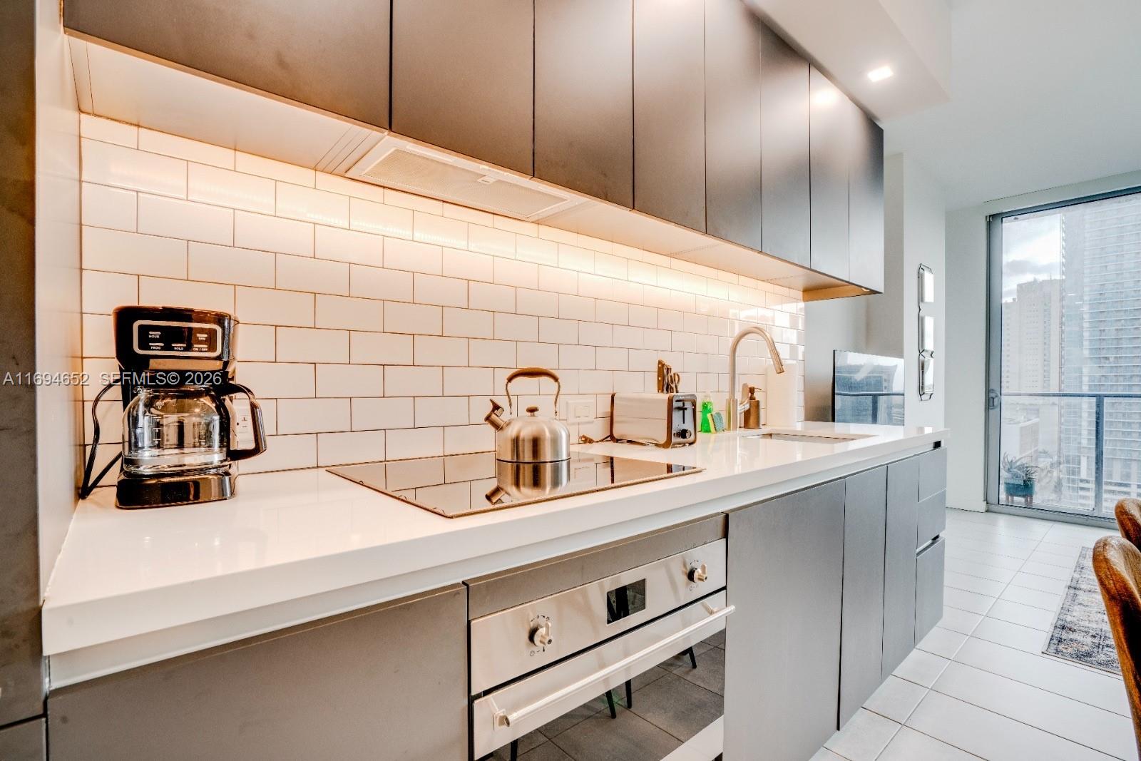 A modern kitchen features dark gray cabinetry, white subway tile backsplash, and stainless steel appliances — 227 NE 2nd St # 1705, Miami FL 33132, MIAMI, FL