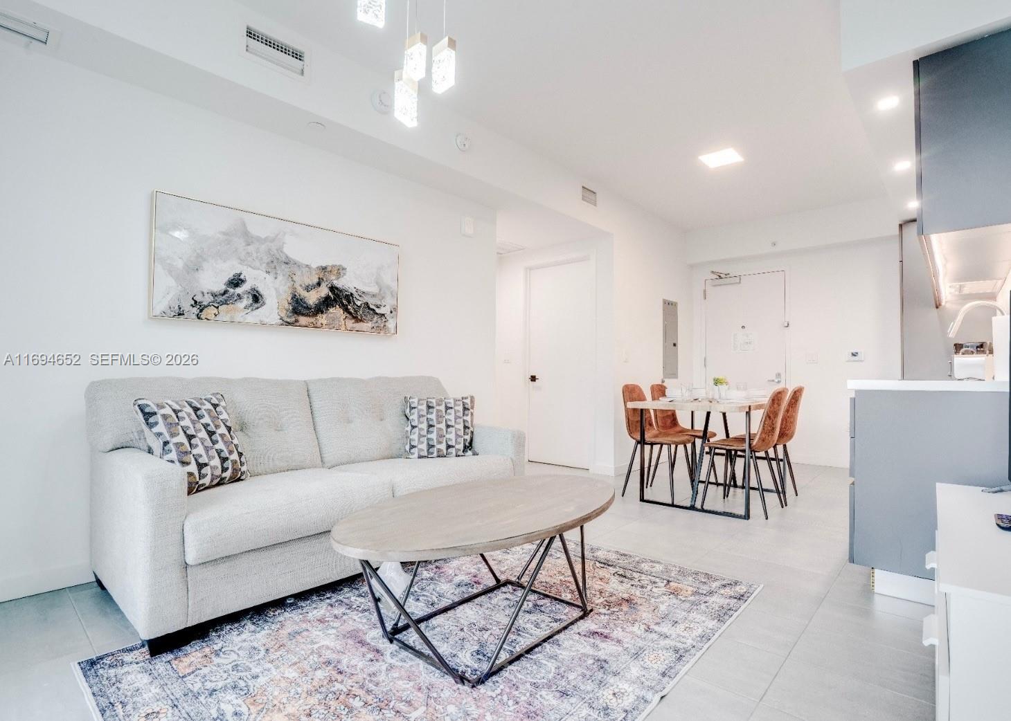 A modern living room features a light gray sofa, oval coffee table, and dining area — 227 NE 2nd St # 1705, Miami FL 33132, MIAMI, FL