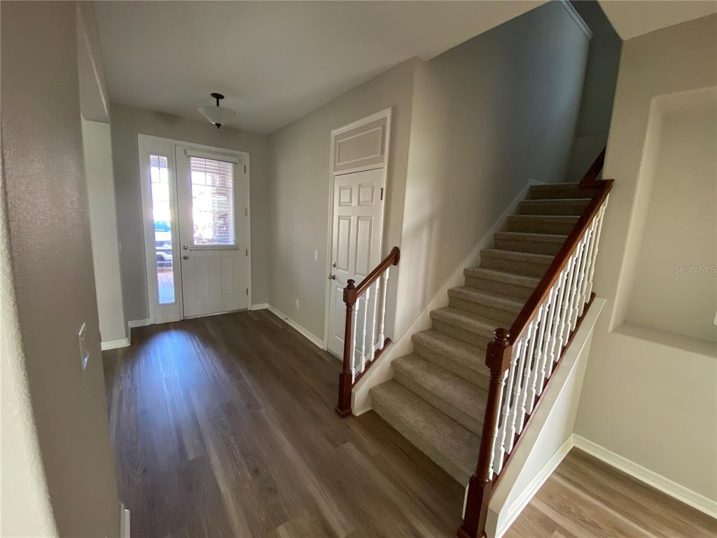 A spacious, empty room with light gray walls and wood-look flooring features a dining area — 4408 BREEZE ISLE LANE, KISSIMMEE, FL