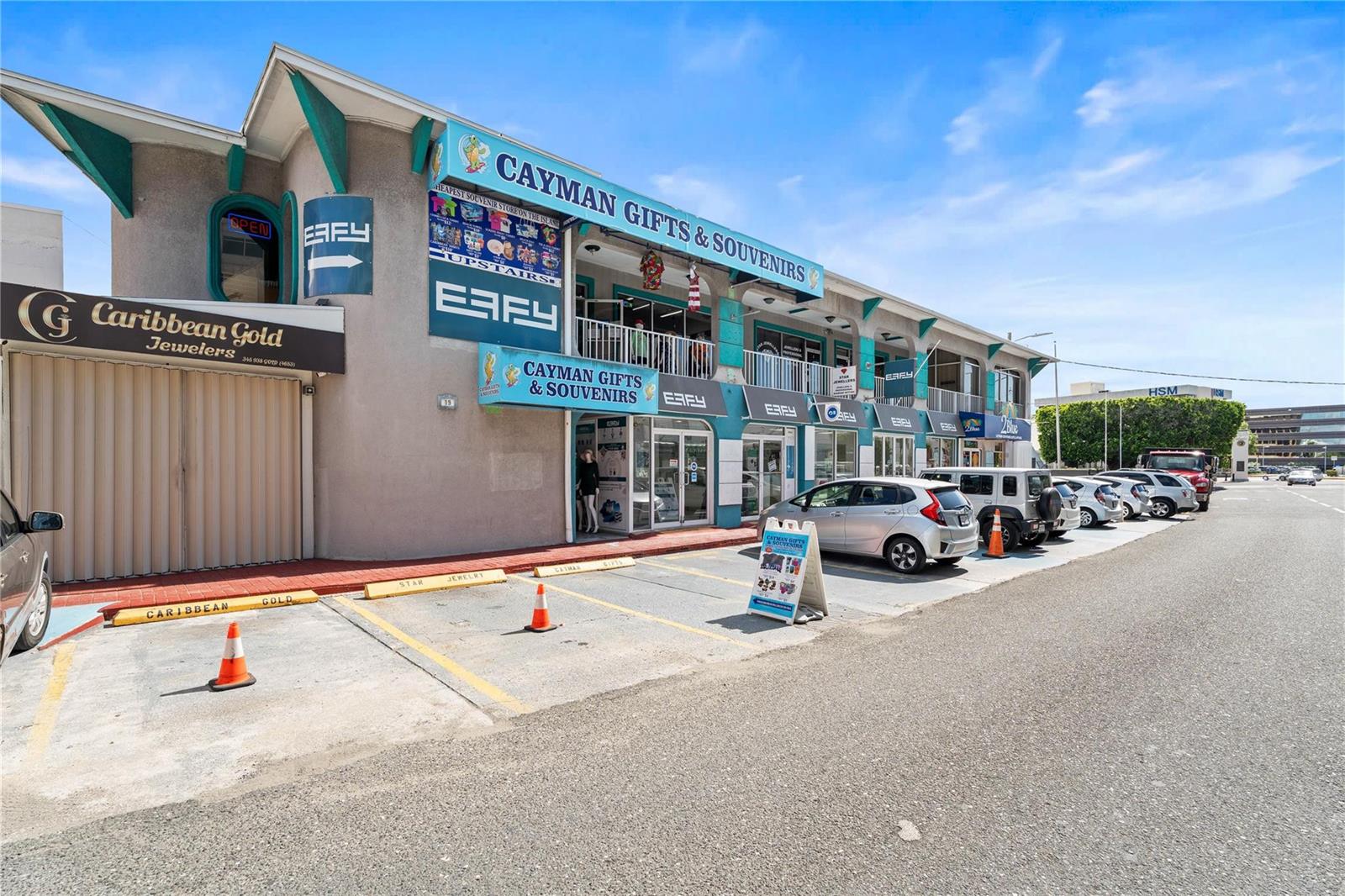 A two-story commercial building with retail storefronts, parking spaces, and signage in a sunny setting — 19 Fort Street, GC, FL
