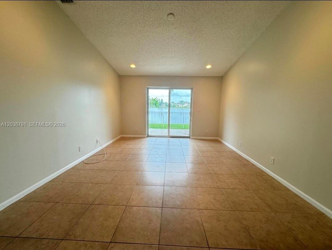 An empty room features beige tile flooring, light-colored walls, and sliding glass doors overlooking water — LAKE WORTH, FL