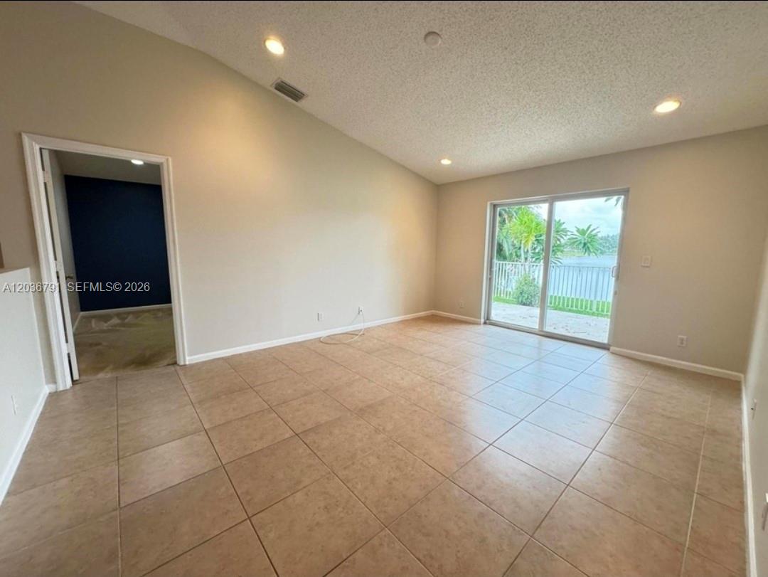 An empty room with beige tile flooring, a vaulted ceiling, and sliding glass doors — LAKE WORTH, FL