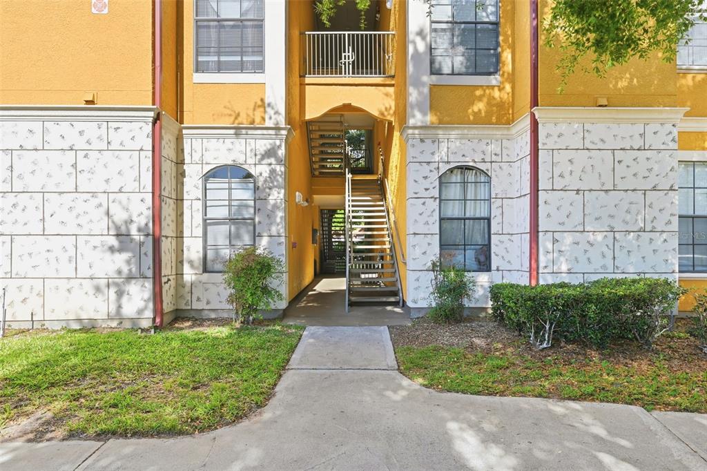 An exterior view of an apartment building entrance with a concrete walkway and metal stairs — 6169 METROWEST BOULEVARD UNIT 305, ORLANDO, FL