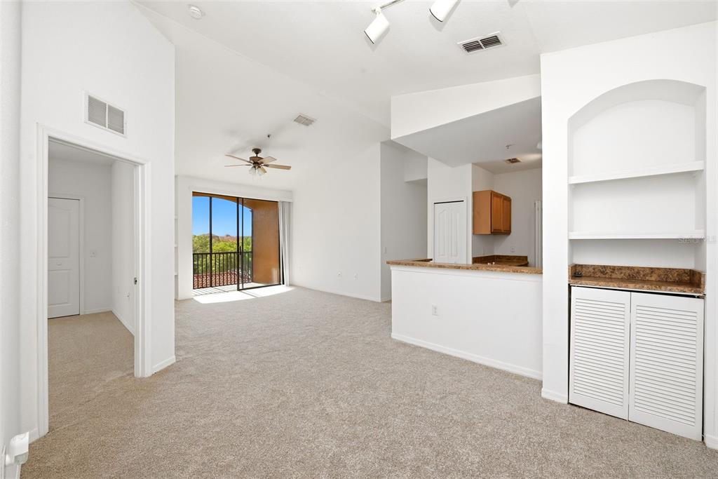 An open-concept living area features beige carpeting, a breakfast bar, and a balcony with views — 6169 METROWEST BOULEVARD UNIT 305, ORLANDO, FL