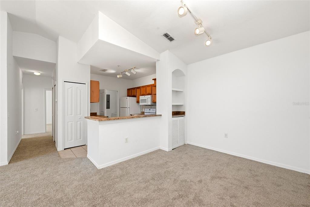 A carpeted living area opens to a kitchen with wooden cabinets and a breakfast bar — 6169 METROWEST BOULEVARD UNIT 305, ORLANDO, FL