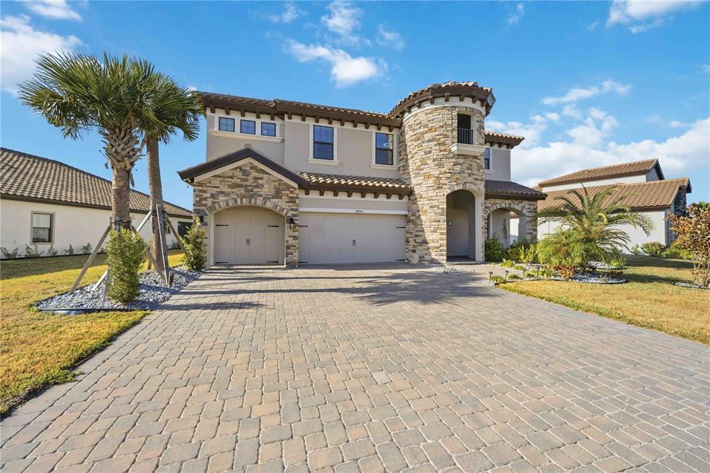 A two-story house with a stone turret, a paved driveway, and a three-car garage — 13845 HEARTWOOD WAY, PARRISH, FL