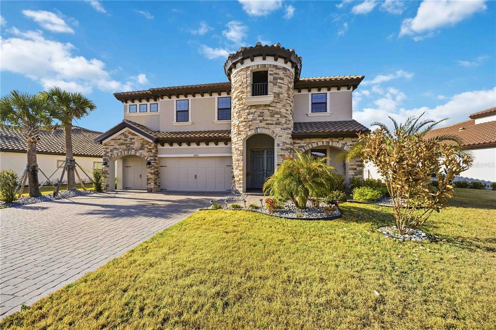 A two-story house with a stone-clad turret, a paved driveway, and palm trees in front — 13845 HEARTWOOD WAY, PARRISH, FL