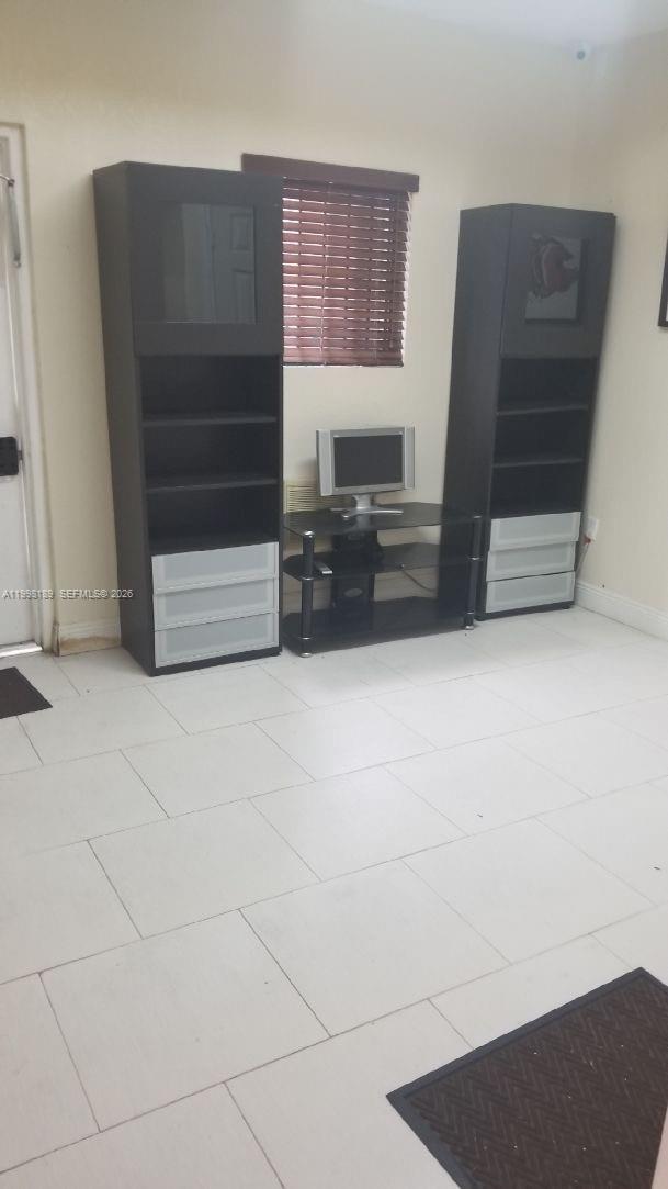 A room features light-colored tile flooring, two tall dark shelving units, and a central television — 1701 W 37th St # 15, Hialeah FL 33012, HIALEAH, FL