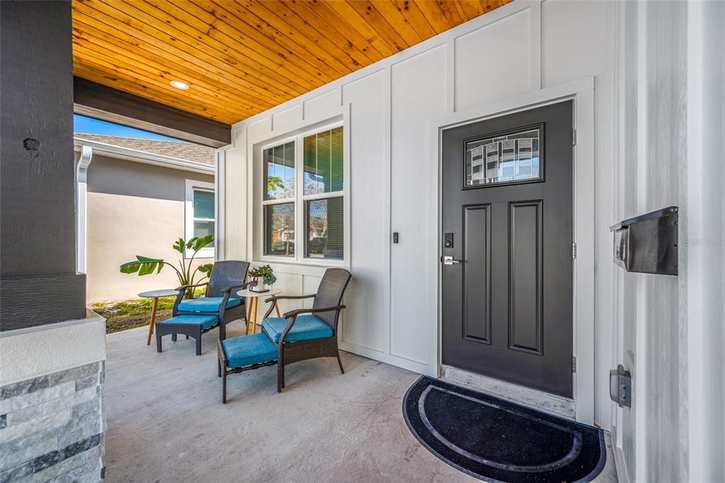 A covered front porch features a black door, two chairs with blue cushions, and wood-paneled ceilings — 2150 43RD TERRACE N, ST PETERSBURG, FL