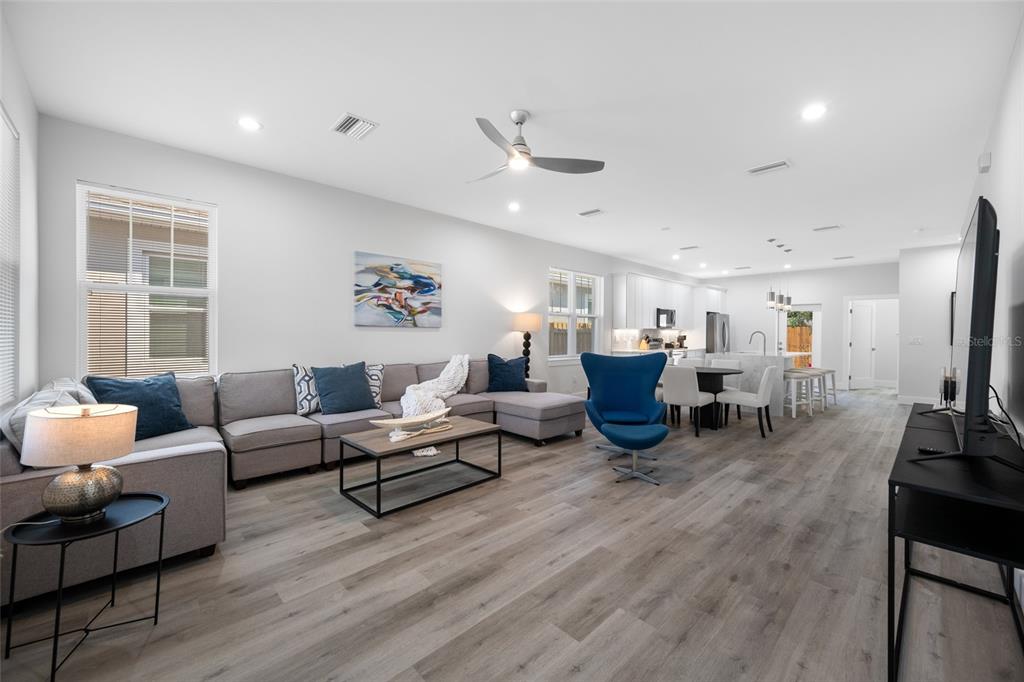 An open-concept living room and kitchen feature light wood flooring, a gray sectional, and white cabinetry — 2150 43RD TERRACE N, ST PETERSBURG, FL