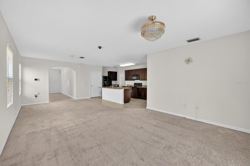 A spacious living room with beige carpet opens to a kitchen with dark wood cabinets — 4842 SAN PALERMO DRIVE, BRADENTON, FL