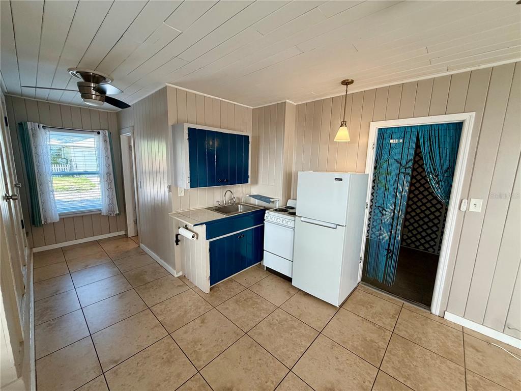 A kitchen features blue cabinets, white appliances, tan tile flooring, and light-colored wood paneling — 3452 9TH AVENUE N UNIT Lower, ST PETERSBURG, FL