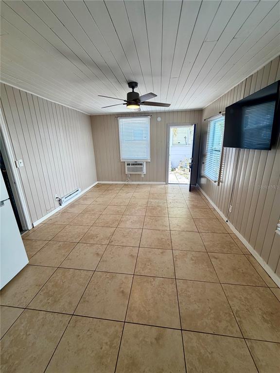 A room with beige tile flooring, wood-paneled walls, a ceiling fan, and a wall-mounted television — 3452 9TH AVENUE N UNIT Lower, ST PETERSBURG, FL