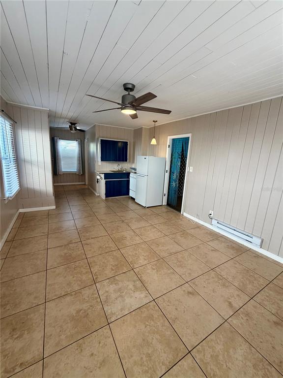 A room with tan tile flooring, wood-paneled walls, a white ceiling, and a small kitchen area — 3452 9TH AVENUE N UNIT Lower, ST PETERSBURG, FL