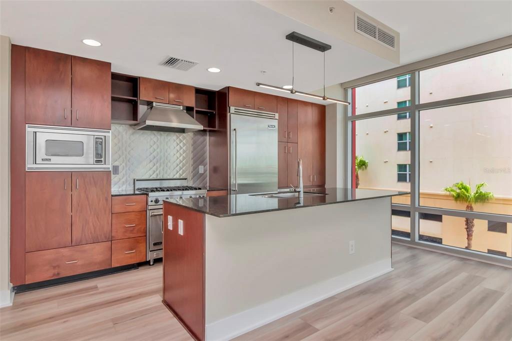 A modern kitchen features wood cabinets, stainless steel appliances, a kitchen island, and floor-to-ceiling windows — 1208 E KENNEDY BOULEVARD UNIT 419, TAMPA, FL