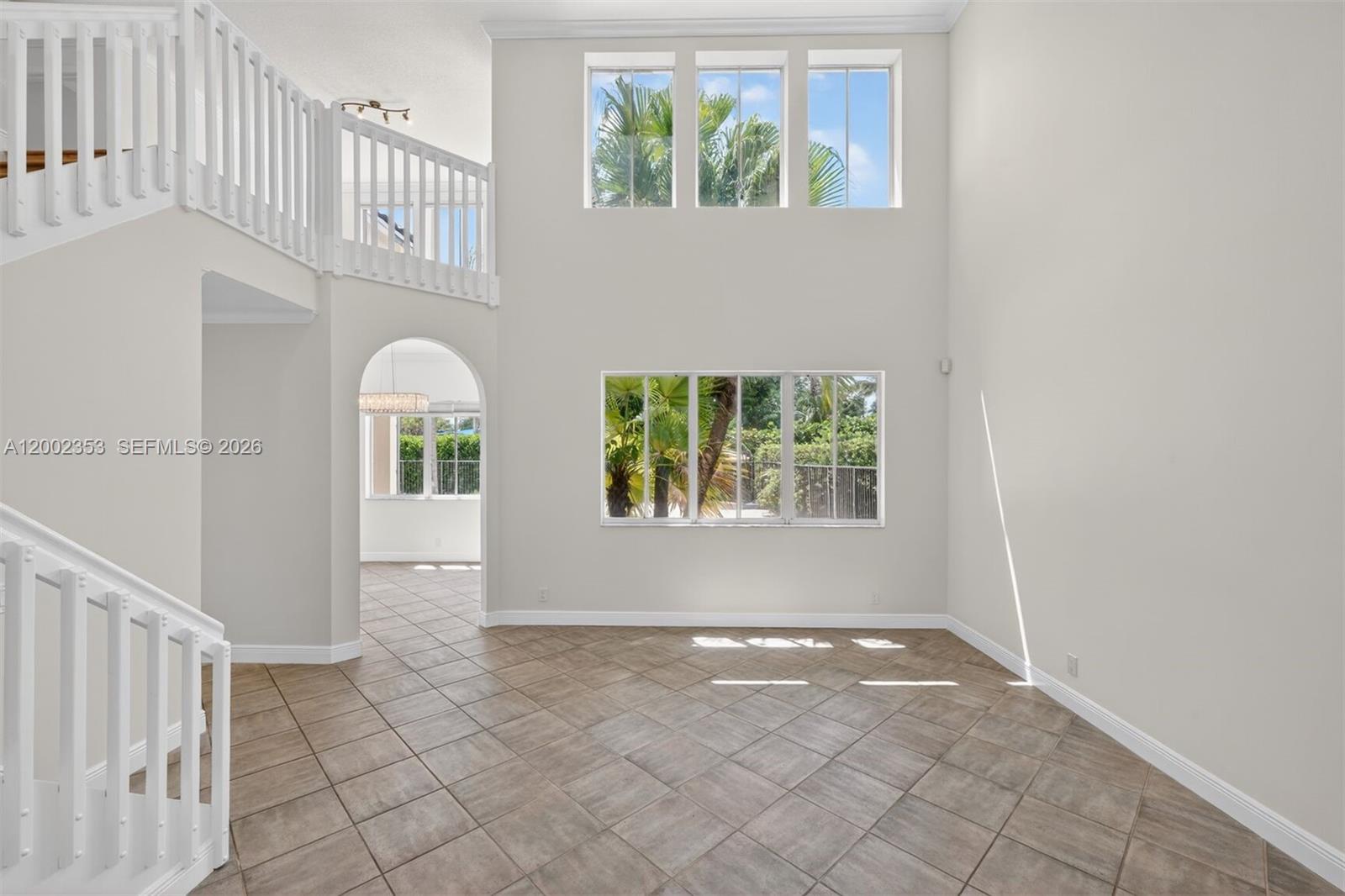 A two-story living room with tile floors, white railings, and large windows overlooking palm trees — 1115 Camellia Cir, Weston FL 33326, WESTON, FL