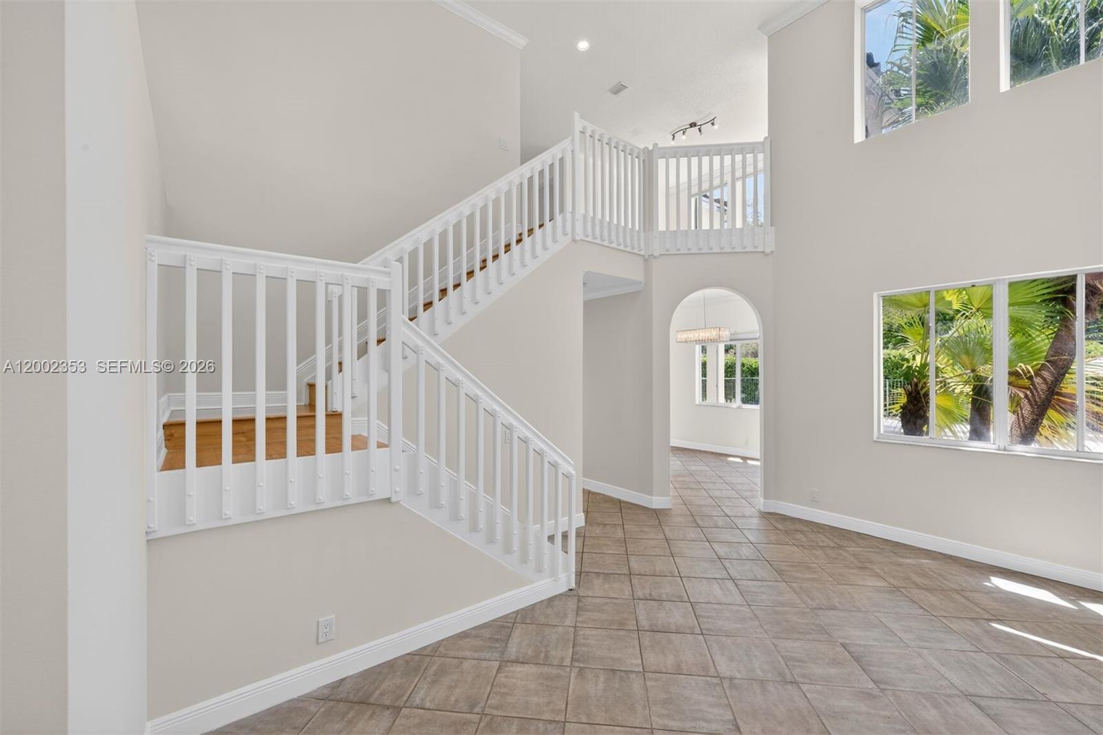 A bright foyer features a white staircase, tiled floors, and an arched entryway — 1115 Camellia Cir, Weston FL 33326, WESTON, FL