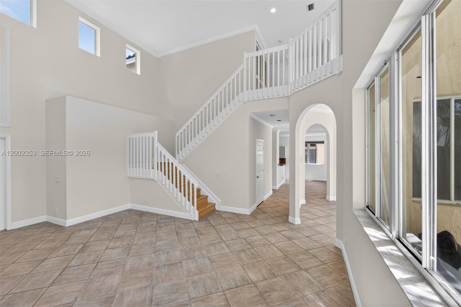 A high-ceilinged room features tiled floors, a wooden staircase, and an arched entryway — 1115 Camellia Cir, Weston FL 33326, WESTON, FL
