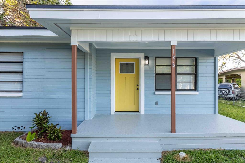 The exterior of a light blue house features a yellow front door and a covered porch — 136 TAYLOR AVENUE, DAYTONA BEACH, FL