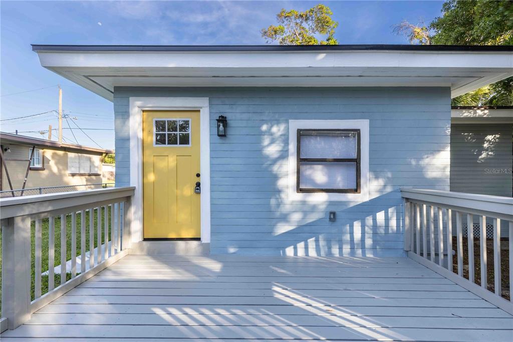A light blue house exterior features a yellow front door and a wooden deck — 136 TAYLOR AVENUE, DAYTONA BEACH, FL