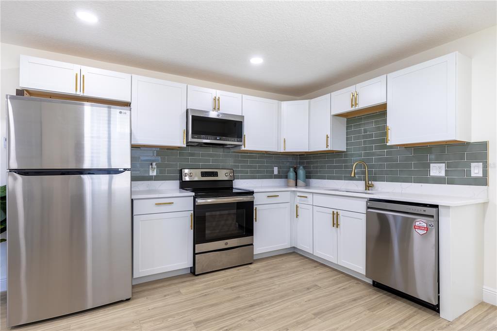 A kitchen features white cabinets, stainless steel appliances, and a green subway tile backsplash — 136 TAYLOR AVENUE, DAYTONA BEACH, FL