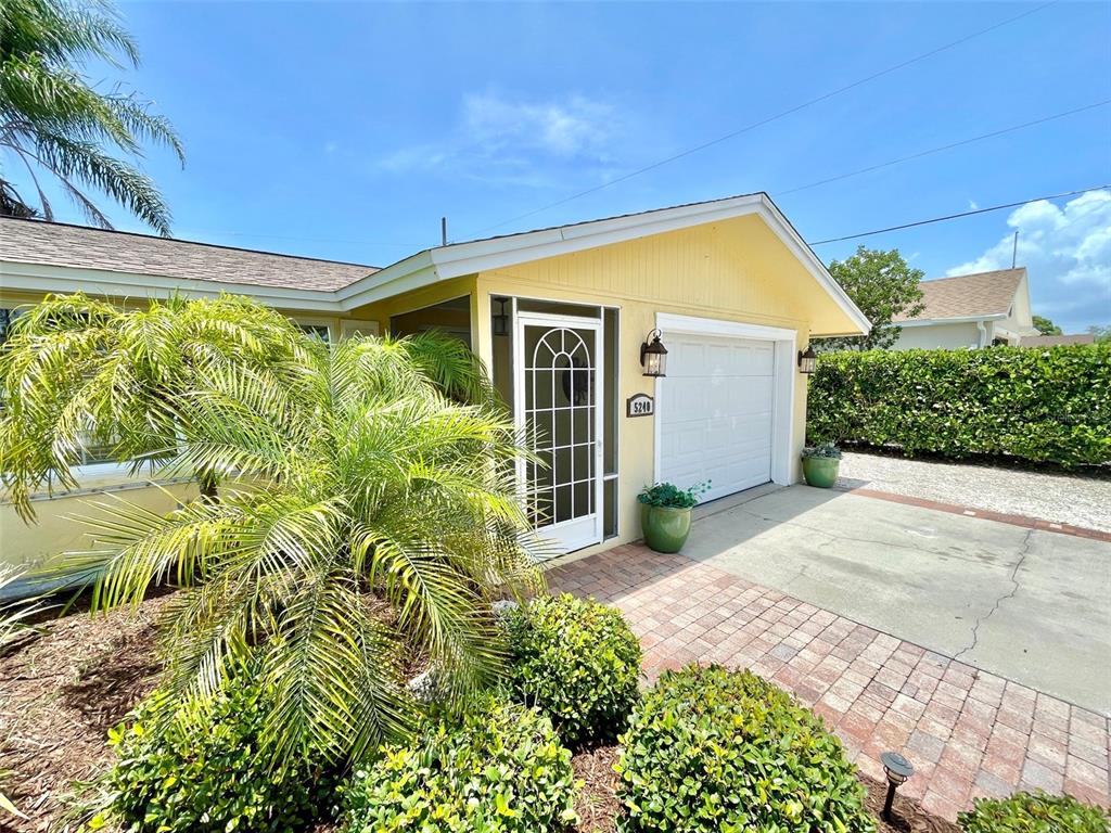 A yellow house exterior features a white garage door, a screened entryway, and landscaping — 5240 DREW ROAD, VENICE, FL