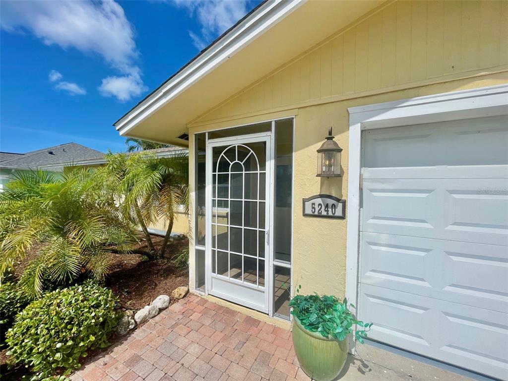 A yellow house exterior features a white storm door, a garage, and a potted plant — 5240 DREW ROAD, VENICE, FL