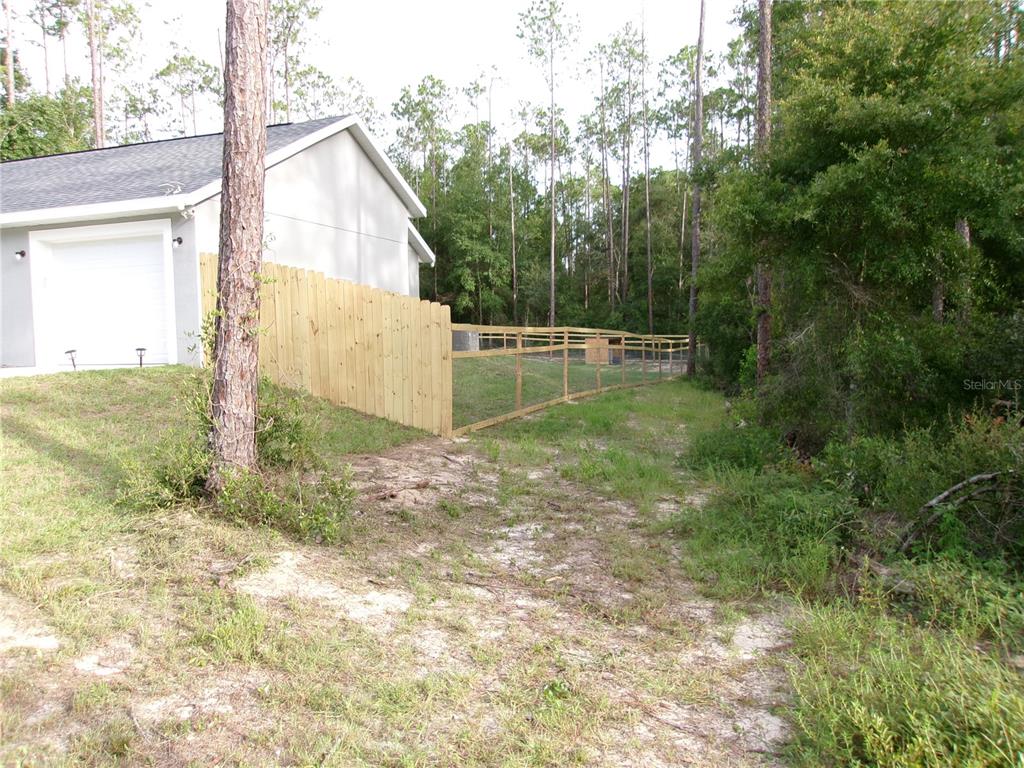 A wooden fence encloses a grassy backyard next to a house with a white garage — LOT 20 SW RAINBOW LAKES BOULEVARD, DUNNELLON, FL