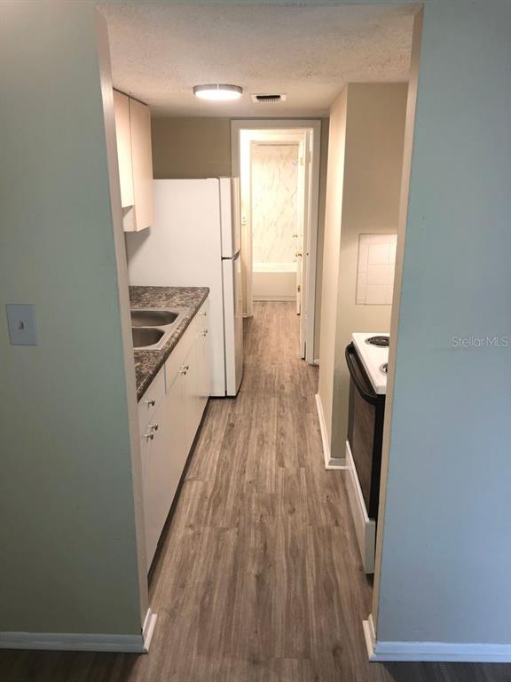 A narrow kitchen features white cabinets, a refrigerator, a stove, and wood-look flooring — 1311 BAYWATCH LOOP UNIT 204, TAMPA, FL