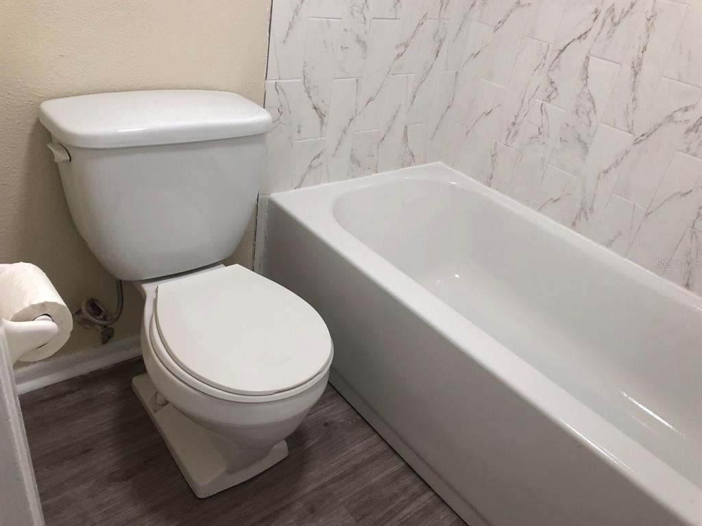 A white toilet sits next to a bathtub with white marble-patterned wall tiles — 1311 BAYWATCH LOOP UNIT 204, TAMPA, FL
