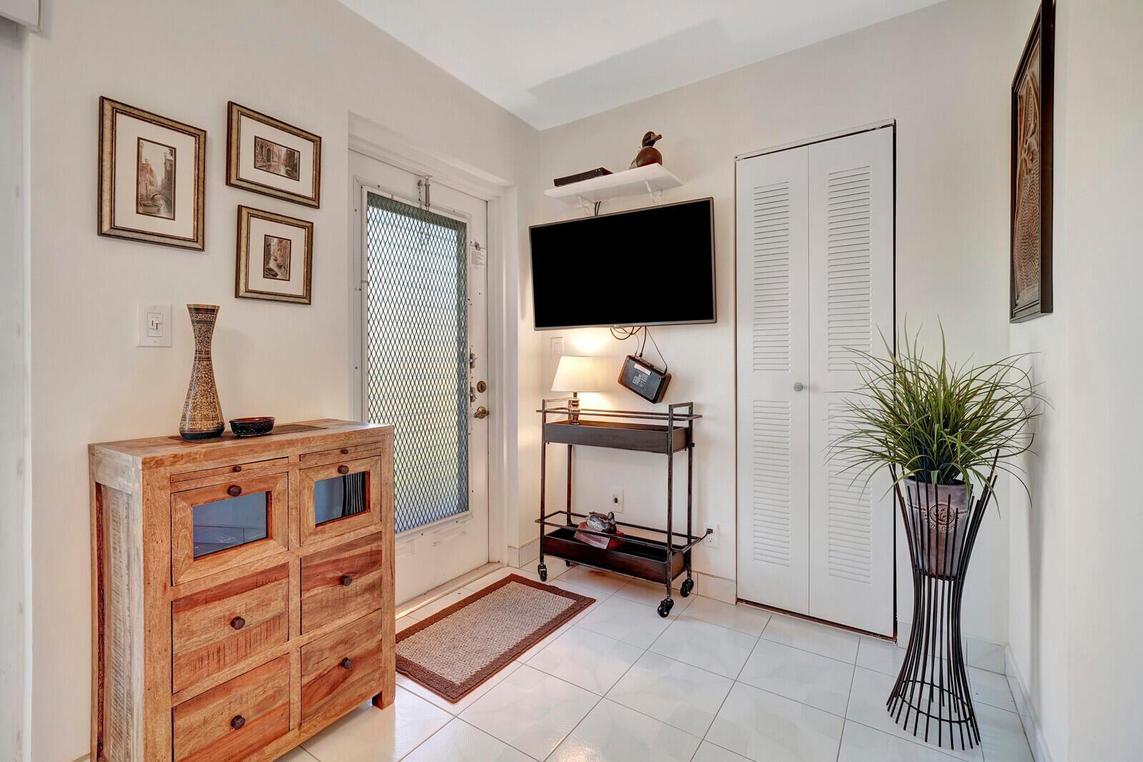 An entryway features a wooden cabinet, a rolling bar cart with a television, and a closet — 7547 S Oriole Boulevard # 202, Delray Beach FL 33446, DELRAY BEACH, FL