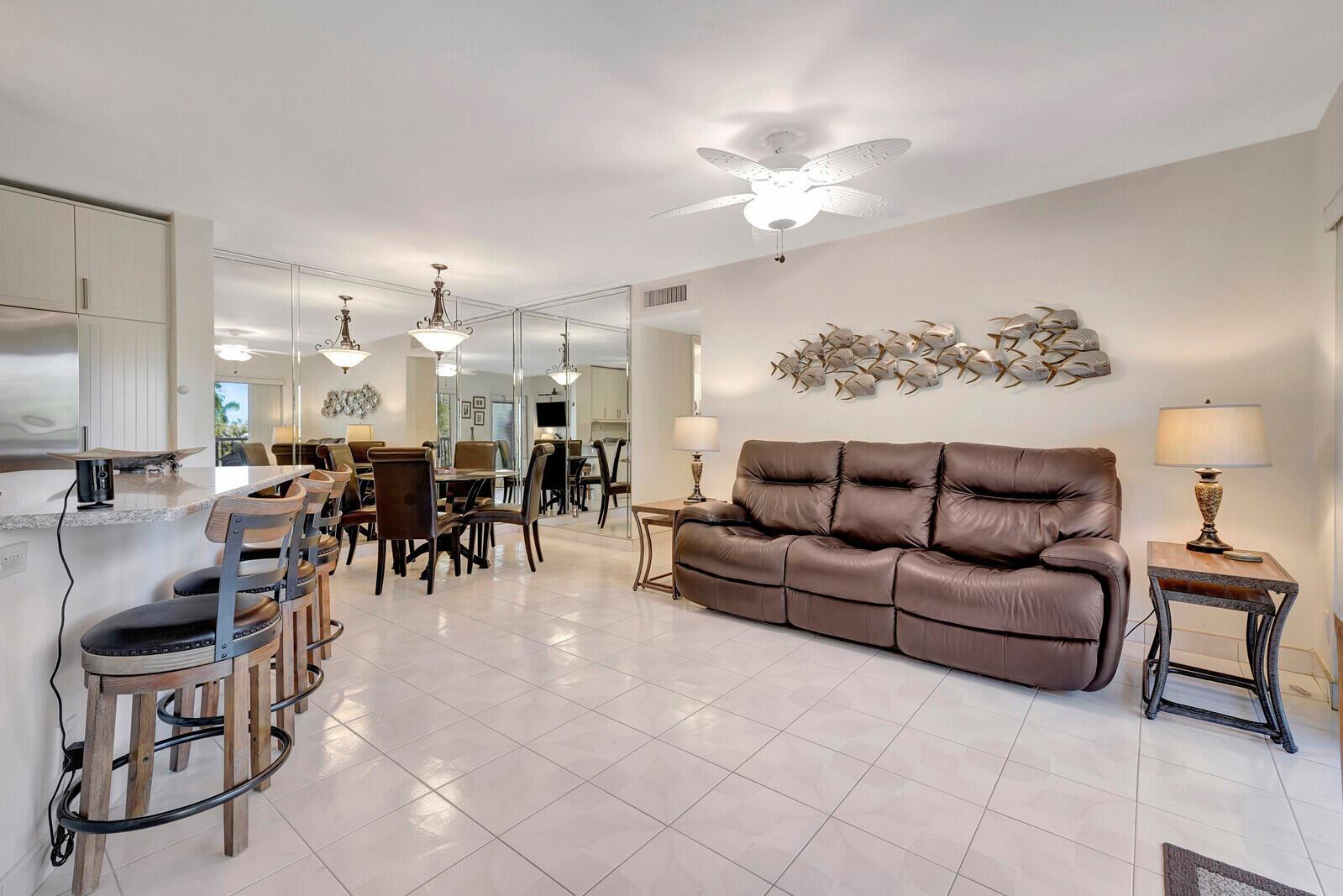 A living room and dining area with tile floors, a brown sofa, and mirrored walls — 7547 S Oriole Boulevard # 202, Delray Beach FL 33446, DELRAY BEACH, FL