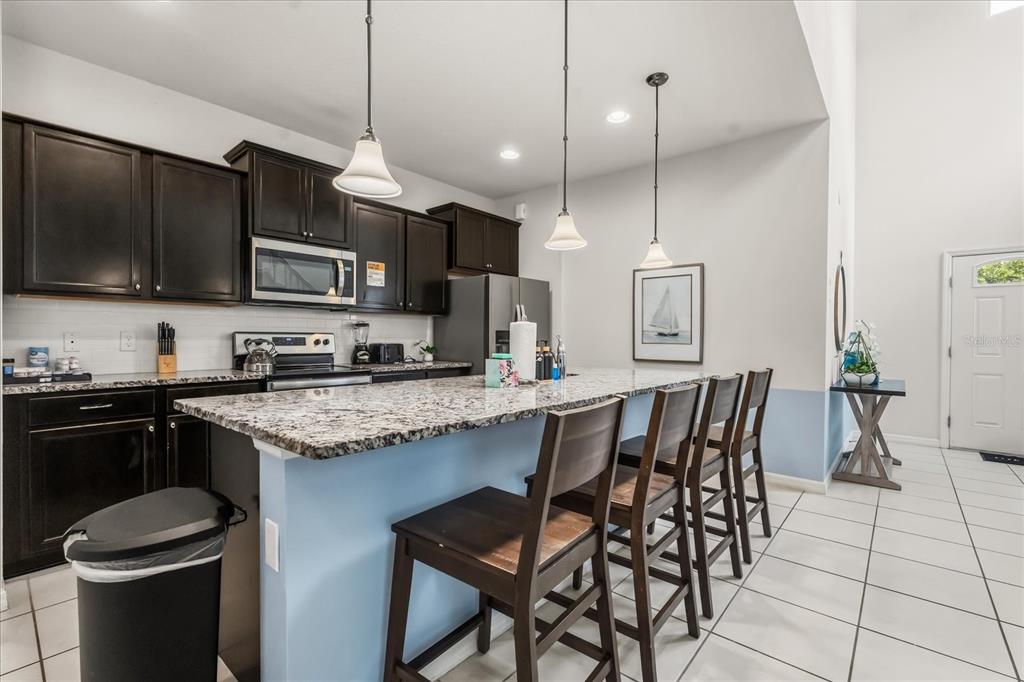 A kitchen features dark wood cabinets, granite countertops, a breakfast bar, and three pendant lights — 8908 PRAGUE WAY, KISSIMMEE, FL
