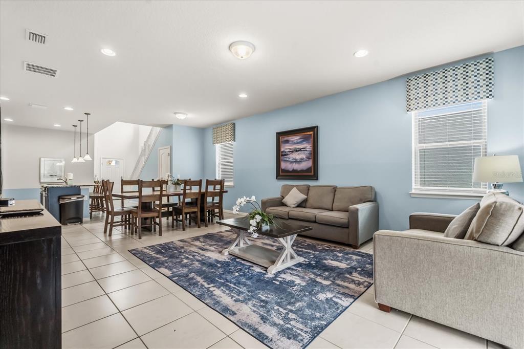 An open-concept living and dining area features light blue walls, tile flooring, and neutral furniture — 8908 PRAGUE WAY, KISSIMMEE, FL