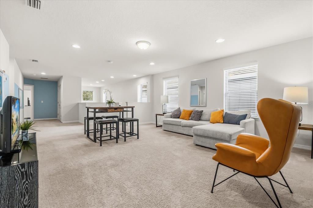 A spacious carpeted living area features a gray sectional sofa, an orange accent chair, and table — 8908 PRAGUE WAY, KISSIMMEE, FL