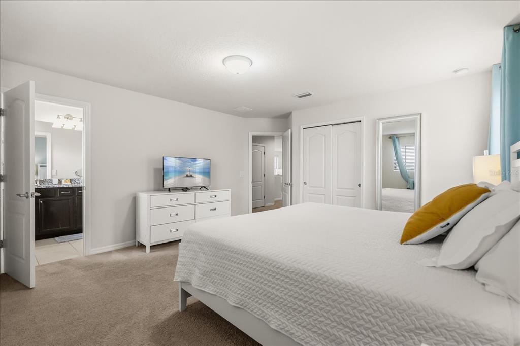 A bedroom with a white dresser, a television, a bed, and an attached bathroom — 8908 PRAGUE WAY, KISSIMMEE, FL