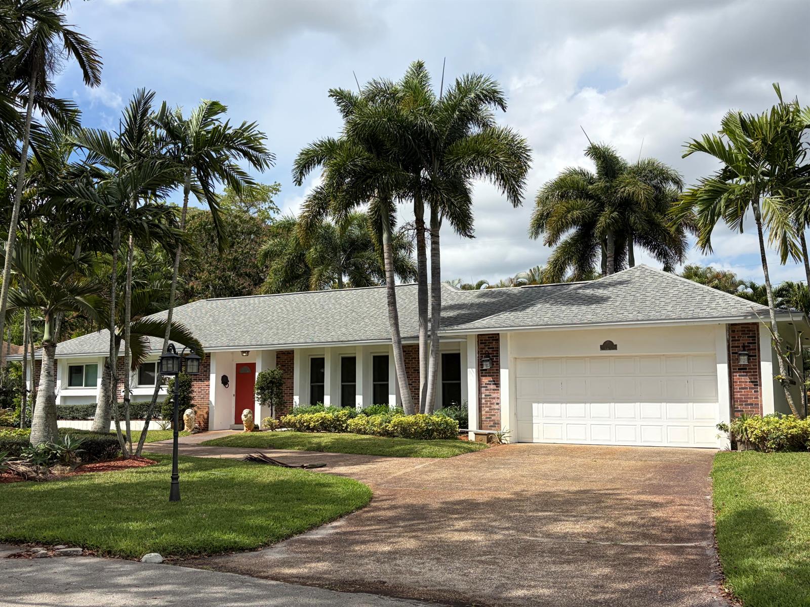 A single-story brick house with a white garage, red front door, and tall palm trees — 8 Bell Lane, Palm Springs FL 33406, PALM SPRINGS, FL