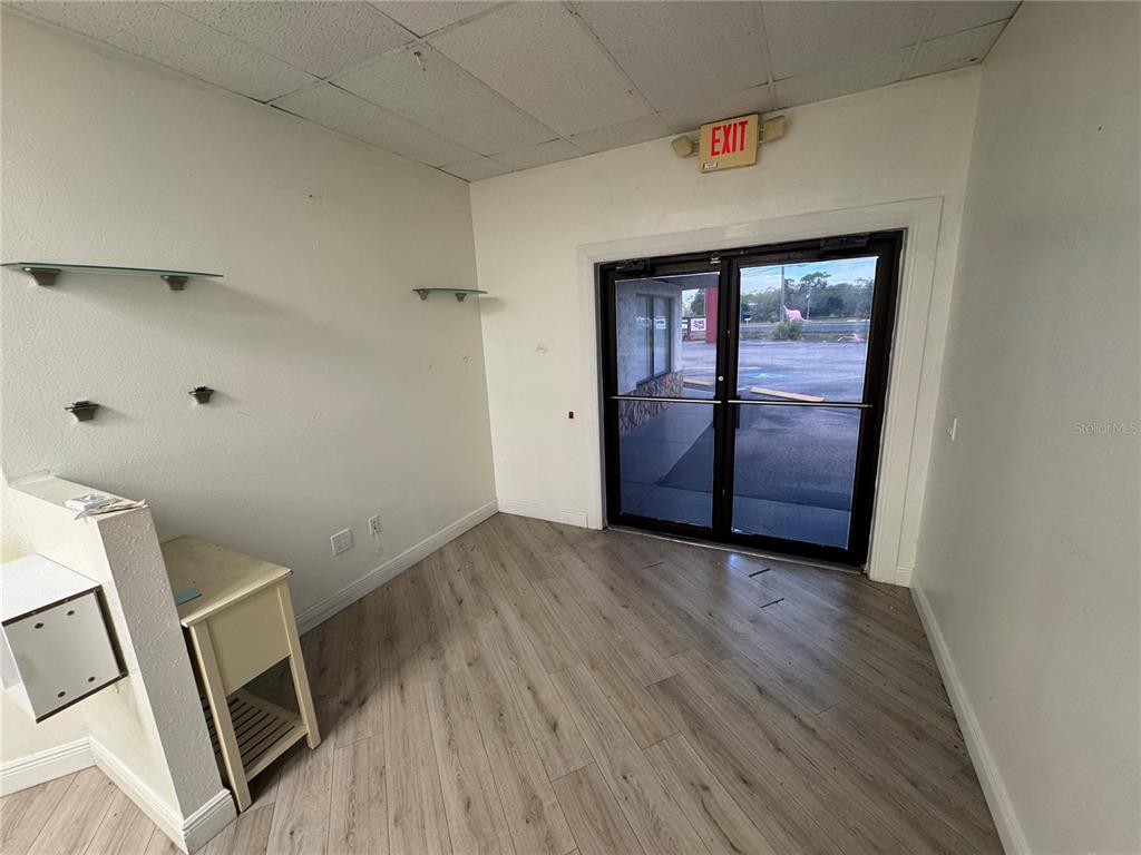 An empty commercial room features light wood-look flooring, white walls, glass shelves, and double glass doors — 3274 COMMERCIAL WAY, SPRING HILL, FL