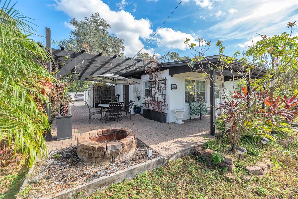 A patio features a stone fire pit, a pergola, and outdoor furniture next to a house — 105 S SAINT CLOUD AVENUE, VALRICO, FL