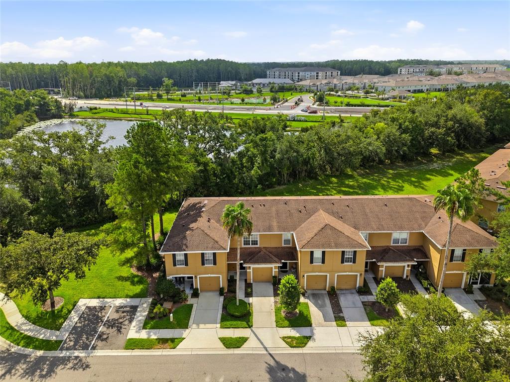 An aerial view shows a multi-unit townhouse building with garages and a nearby pond — 4610 WINDING RIVER WAY, LAND O LAKES, FL