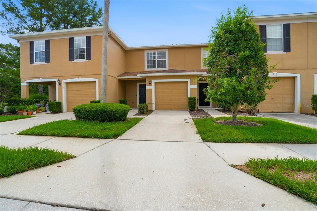 A tan two-story townhouse exterior features three garage doors, a driveway, and front landscaping — 4610 WINDING RIVER WAY, LAND O LAKES, FL