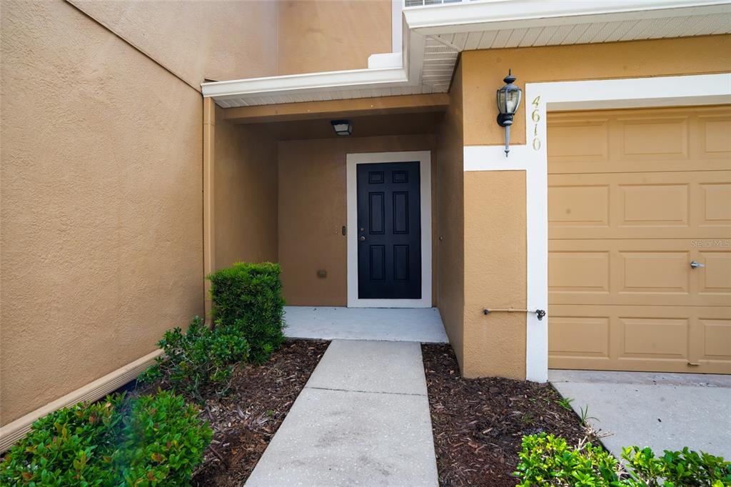 A tan house exterior features a dark front door, a concrete walkway, and a garage — 4610 WINDING RIVER WAY, LAND O LAKES, FL