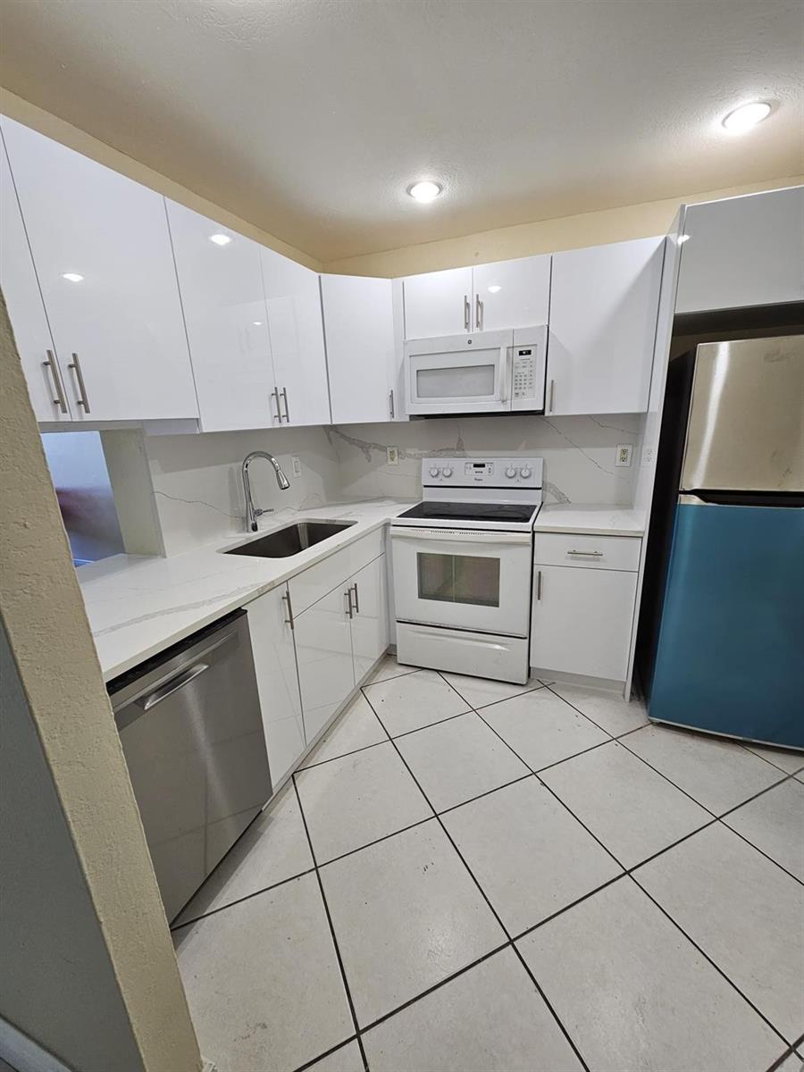A kitchen features white glossy cabinets, stainless steel appliances, and white countertops with gray veining — 5665 W 20th Avenue # 413, Hialeah FL 33012, HIALEAH, FL