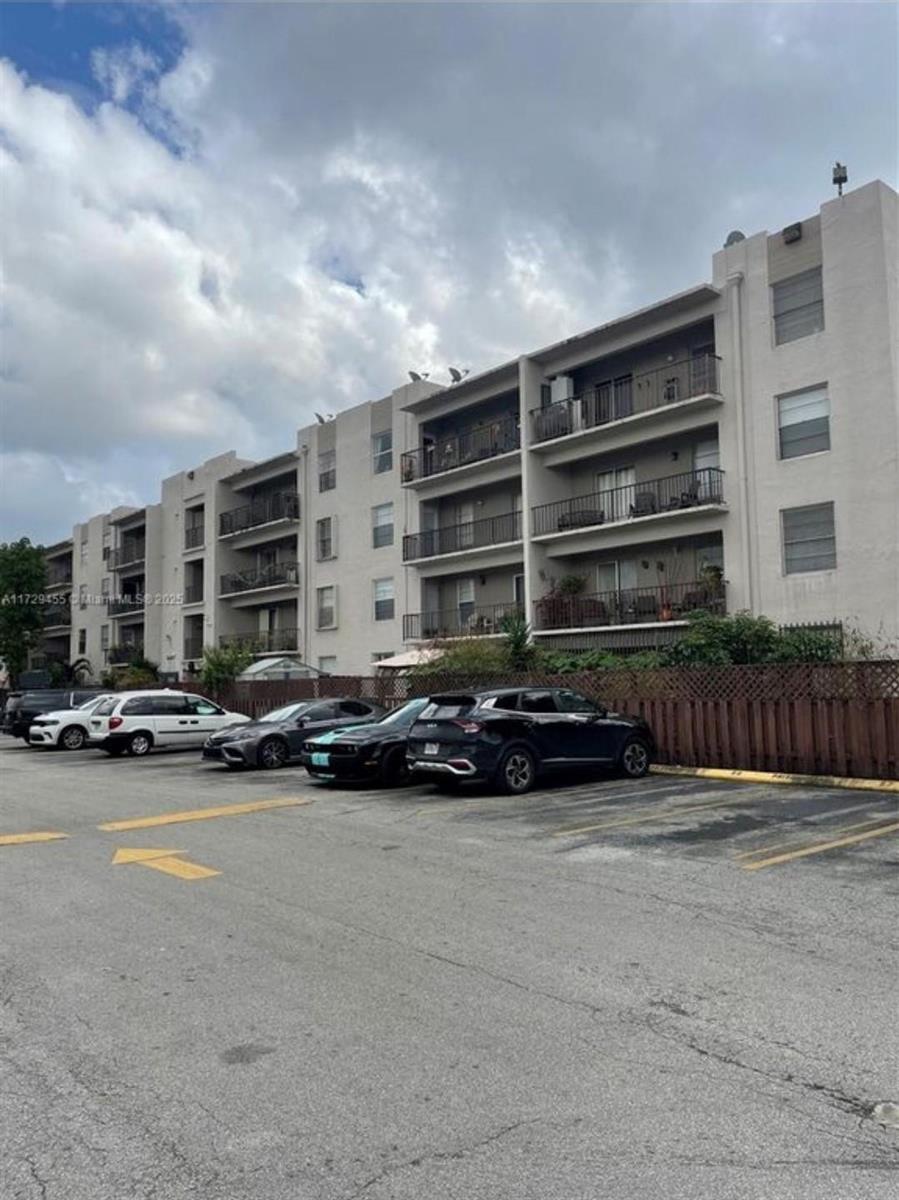 A multi-story apartment building with balconies stands behind a parking lot with several cars — 5665 W 20th Avenue # 413, Hialeah FL 33012, HIALEAH, FL