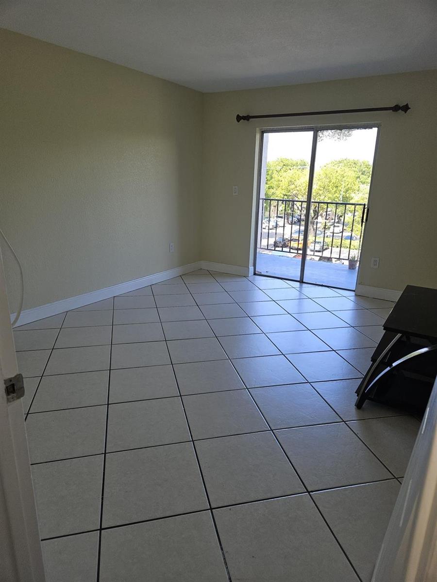 An empty room features beige walls, light-colored tile flooring, and a sliding glass balcony door — 5665 W 20th Avenue # 413, Hialeah FL 33012, HIALEAH, FL