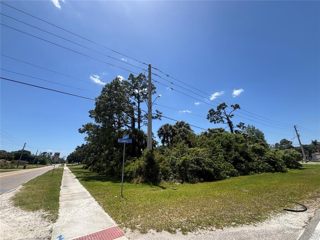 A vacant, tree-covered corner lot sits next to a sidewalk and a paved road — Lot #11 N CHAMBERLAIN BOULEVARD, NORTH PORT, FL