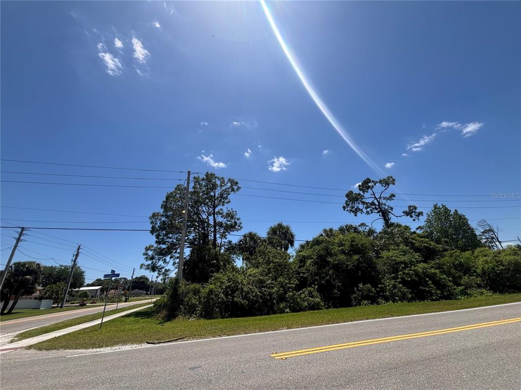 A view of a vacant, wooded corner lot along a paved road under a sunny sky — Lot #11 N CHAMBERLAIN BOULEVARD, NORTH PORT, FL