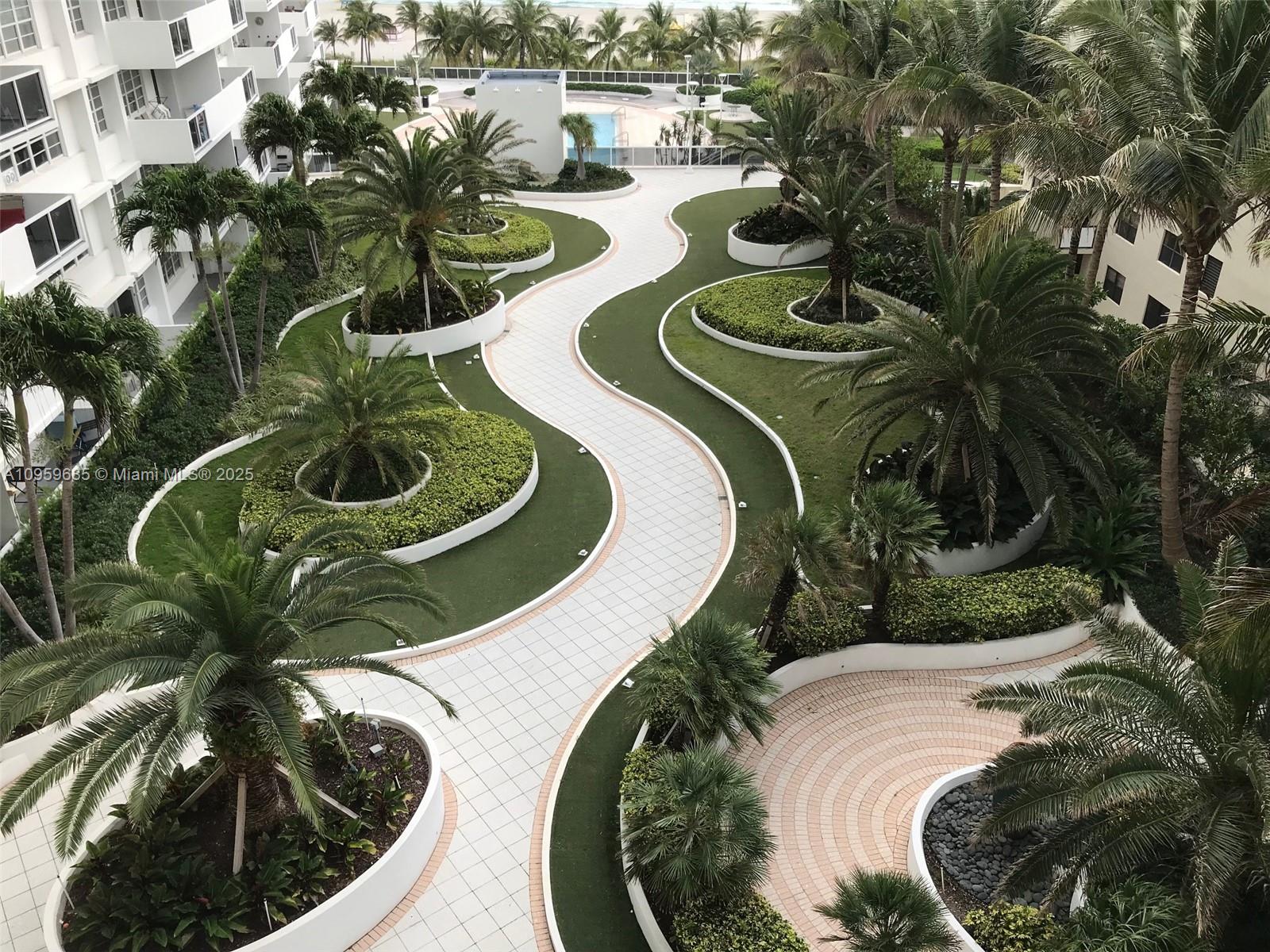 An elevated view of a landscaped courtyard with curved walkways, palm trees, and white planters — 100 Lincoln Rd # 719, Miami Beach FL 33139, MIAMI BEACH, FL